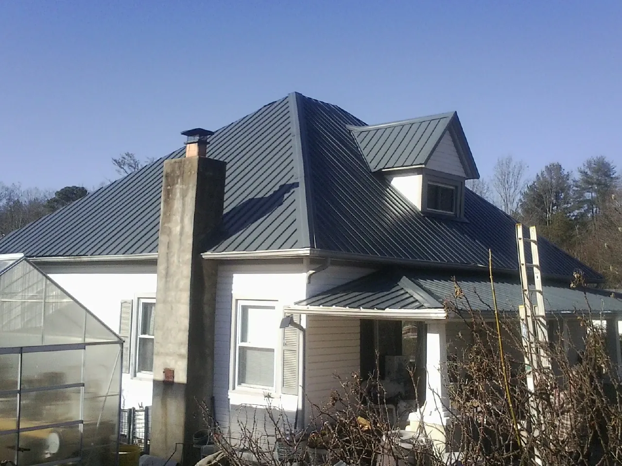 Dark blue standing seam metal roof on a white farmhouse with dormer — Slate & Tile Roof Repair by Roofing Brothers in Big Rock