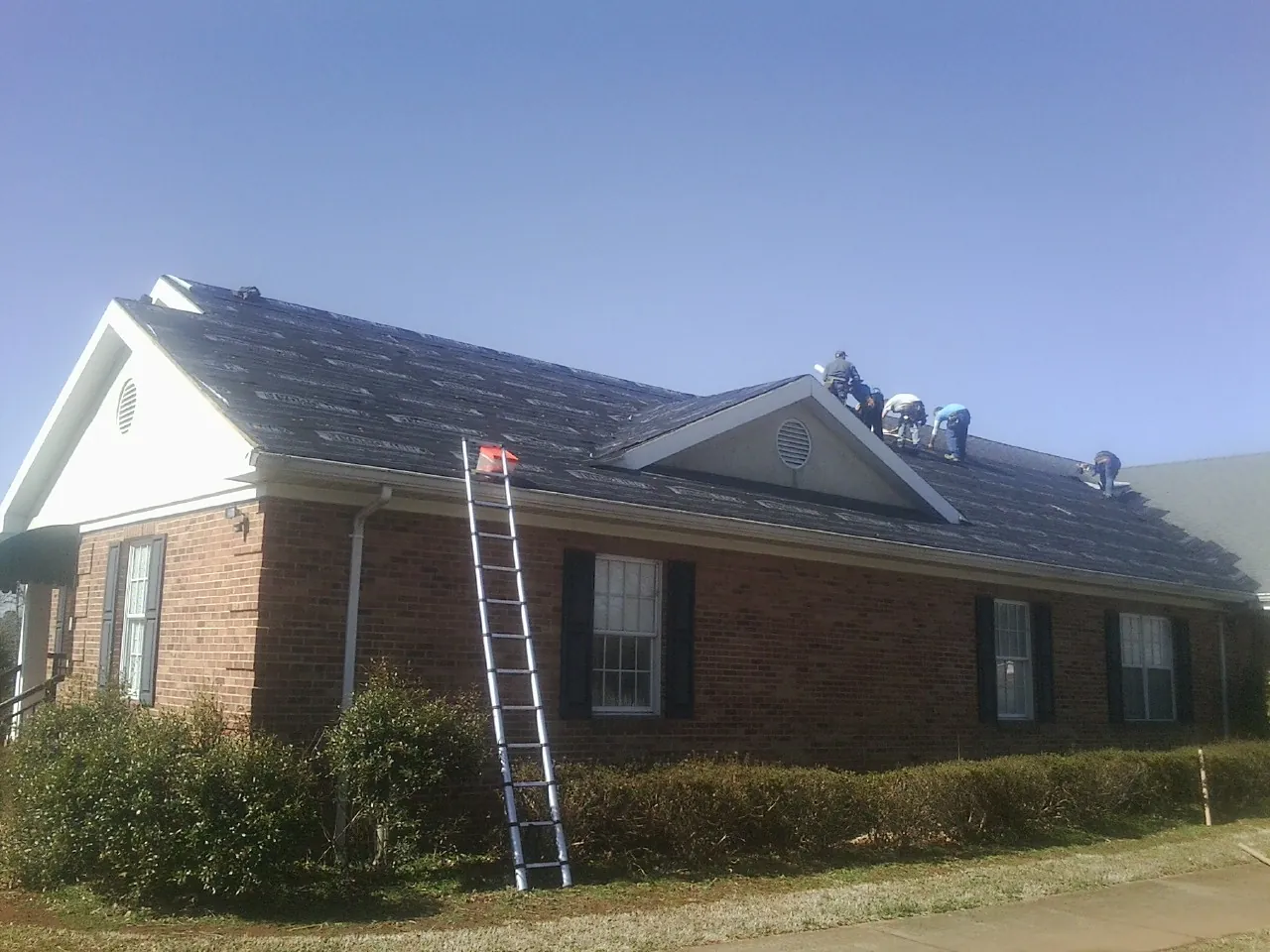 Crew tearing shingles off a brick ranch roof with a ladder set — Emergency Roof Repair work by our crew in Big Rock