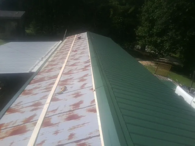 Old rusted panels beside newly installed green metal roofing — Wind Damage Roof Repair by Roofing Brothers in Big Rock