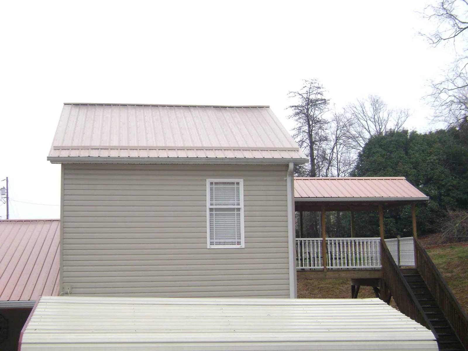 Tan metal roofs on a two story addition and attached porch, from a Roof Replacement job in Big Rock